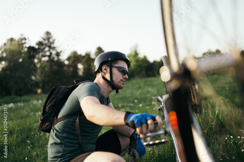 Bike repair. Young man repairing mountain bike in the field