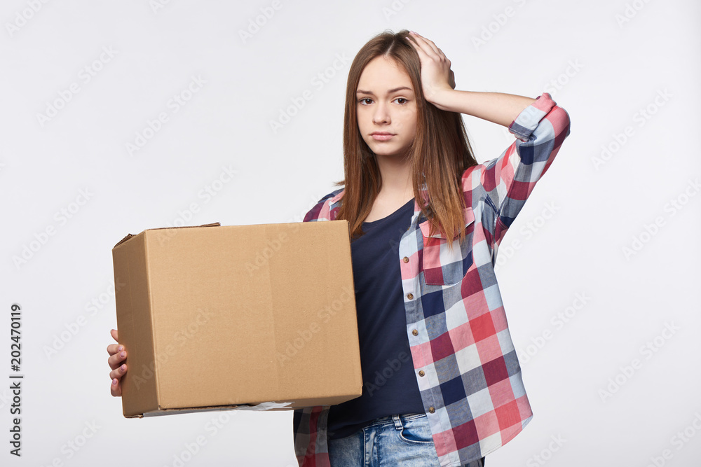 Delivery, relocation and unpacking problems. Discontent young woman holding cardboard box with hand on head Delivery, relocation and unpacking problems. Discontent young woman holding cardboard box with hand on head