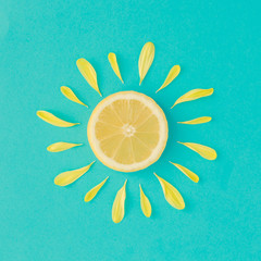Sun made of lemon and yellow flower petals on bright blue background. Fruit summer minimal concept.