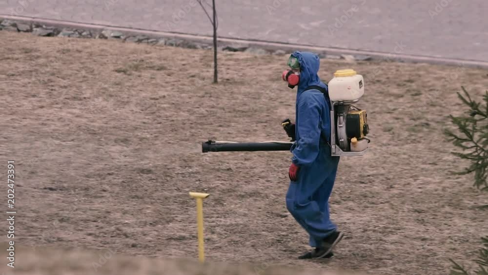 A man in a chemical protection suit and gas mask handles the territory from ticks. A man in a chemical protection suit and gas mask handles the territory from ticks.