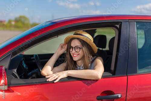 Young woman in car. Girl driving a car. Smiling young woman sitting in red car 