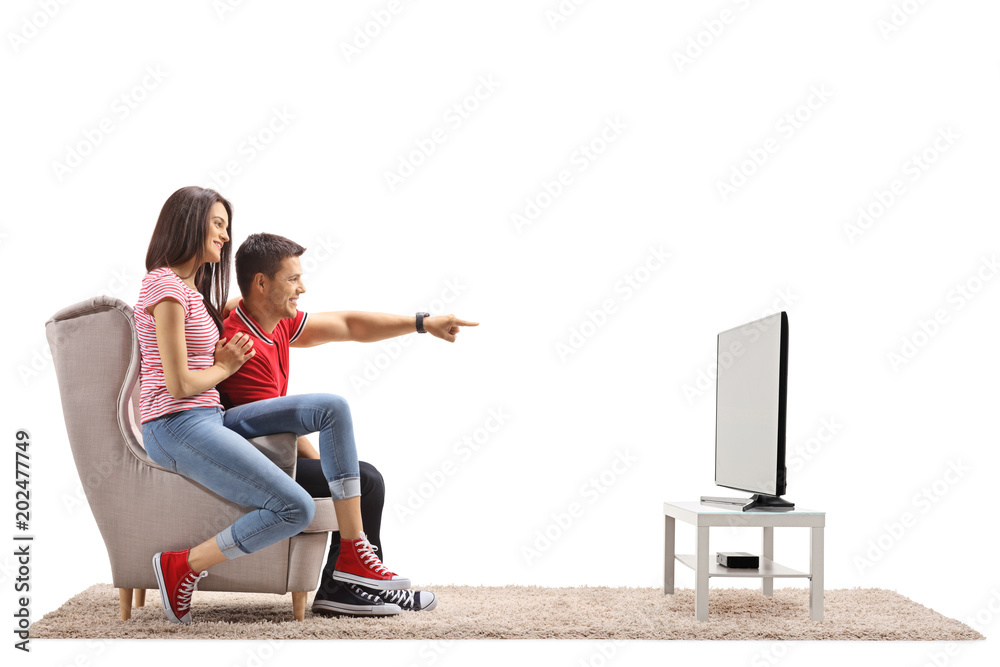 Φωτογραφία Young man and a young woman seated in an armchair watching television with the m