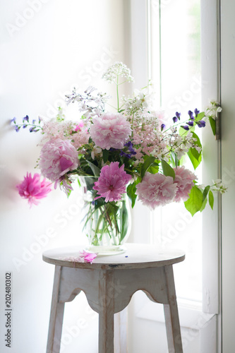A vase of colorful pink and purple flowers sits on a white pedestal next to a window and door. The flowers are fresh  blooming  large  and beautiful.
