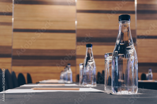 Drinking glasses, plastic water bottles, pencils and papers are prepared for seminar in the hotel meeting room.