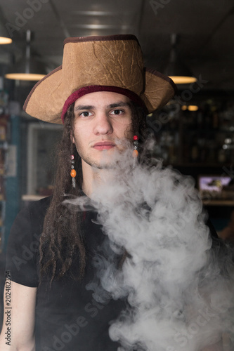 Beautiful young european man wearing a pirate hat and smoking, white heavy smoke