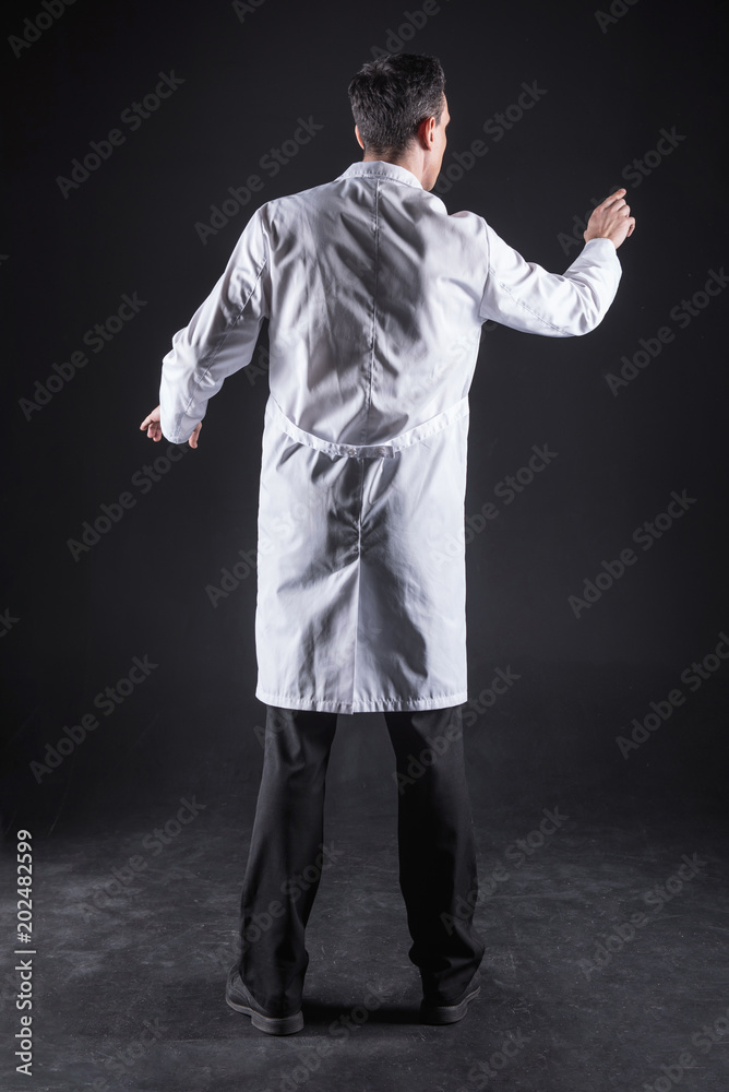 Futuristic innovations. Smart nice pleasant man wearing a labcoat and working in the computer while being in the lab Futuristic innovations. Smart nice pleasant man wearing a labcoat and working in the computer while being in the lab