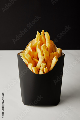 close-up shot of box of french fries on white marble surface isolated on black