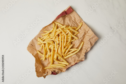 top view of delicious french fries spilled over crumpled paper on white