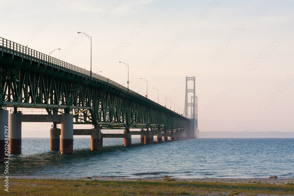 A view from the side of the Mackinac Bridge in Michigan which connects the upper and lower peninsulas. It is sunset, with haze obstructing visibility.