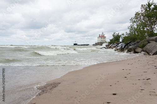 Lighthouse at Mentor Headlands Beach State Park in Ohio with waves crashing on shore and dark clouds overhead.  photo