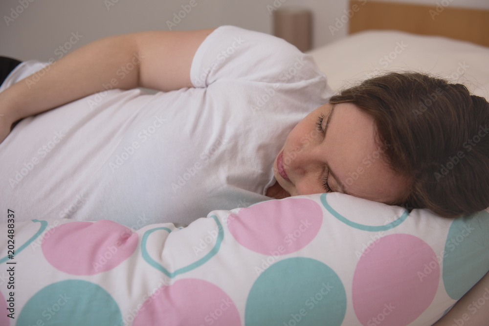 Pregnant woman laying on a bed sleeping with pregnancy pillow Stock