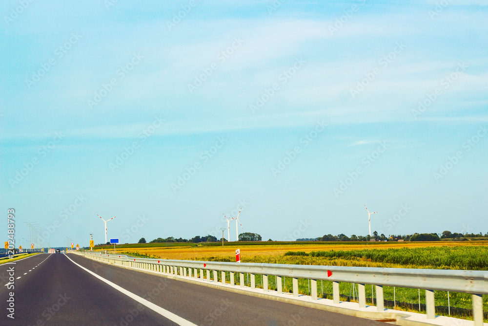Asphalt road, windmills and driving car in distance