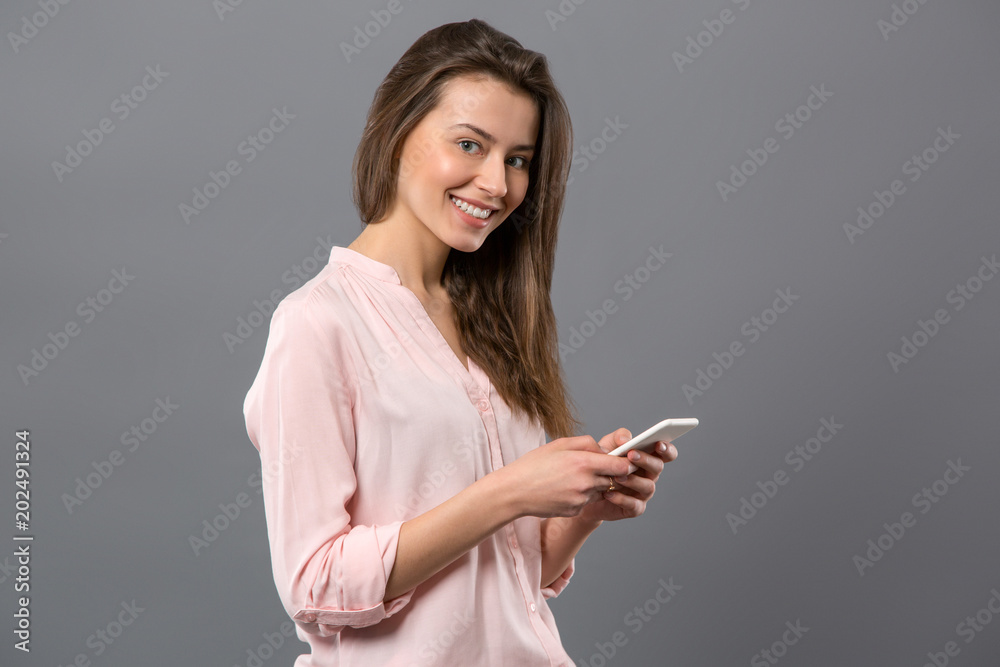 Modern generation. Joyful young woman smiling while using her smartphone Modern generation. Joyful young woman smiling while using her smartphone