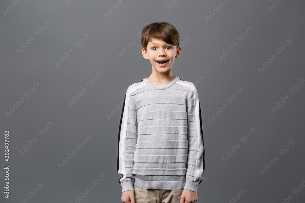 Emotional child. Happy excited boy standing against grey background and looking at you Emotional child. Happy excited boy standing against grey background and looking at you