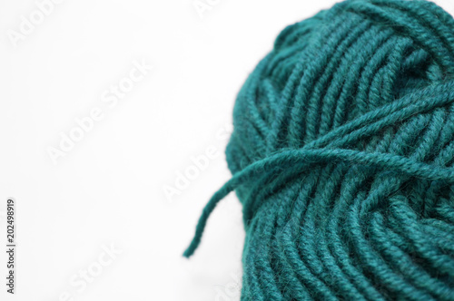 Clew of turquoise knitting wool yarn aside on white surface, handicraft background