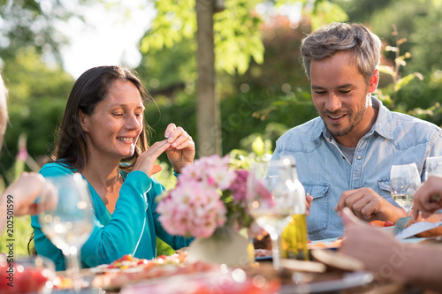 Portrait of a couple in a group of friends gathered around a table in a garden on a summer evening to share a meal and have a good time together
