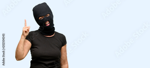 Burglar terrorist woman wearing balaclava ski mask pointing away side with finger isolated blue background