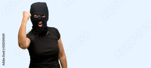Burglar terrorist woman wearing balaclava ski mask irritated and angry expressing negative emotion, annoyed with someone isolated blue background