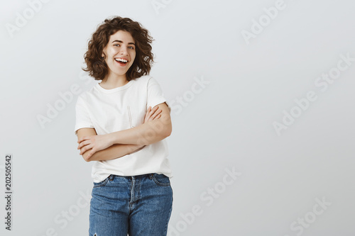 Excellent day to start looking after health. Portrait of positive good-looking european woman with short curly hair, standing with crossed hands and broad smile, taking vitamins to lead active life