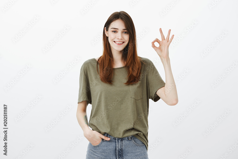No worries, everything is okay. Portrait of confident calm attractive woman in dark-green t-shirt, holding hand in pocket, showing great or ok sign, smiling broadly, assuring she will deal with work