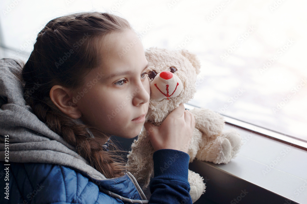 Child girl with a toy bear at the airport near the window looking into the distance. Close-up. Child girl with a toy bear at the airport near the window looking into the distance. Close-up.