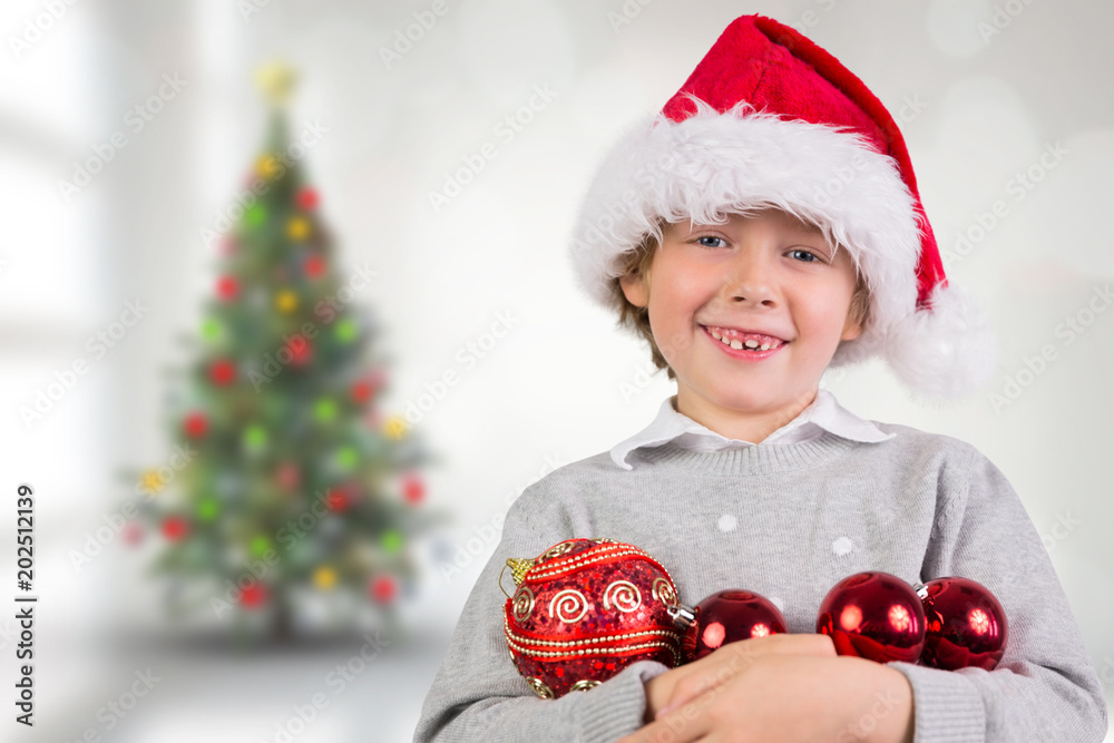 Festive boy smiling against blurry christmas tree in room Festive boy smiling against blurry christmas tree in room