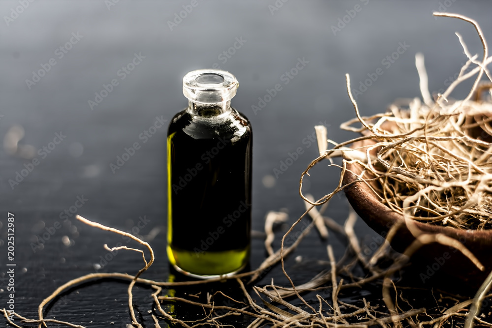 Φωτογραφία Floral and ayurvedic essence of herb Vetiver grass or Khus in a transparent bottle used in many beverages of Indian and Asia with dried vetiver grass in a clay bowl on black surface