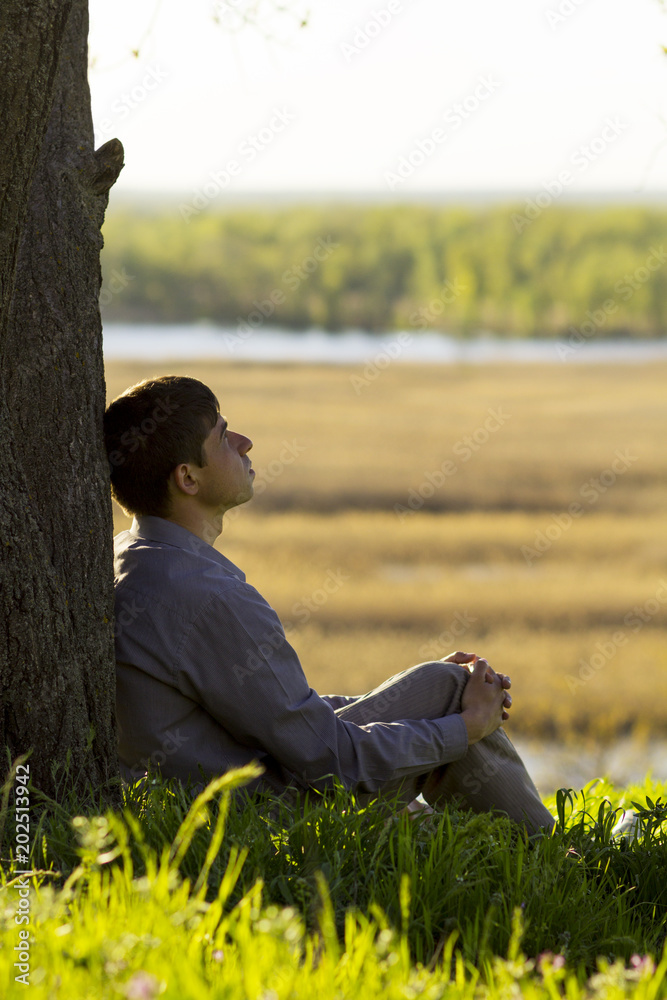 Φωτογραφία young man sitting near tree and meditating, the man spends his time in nature