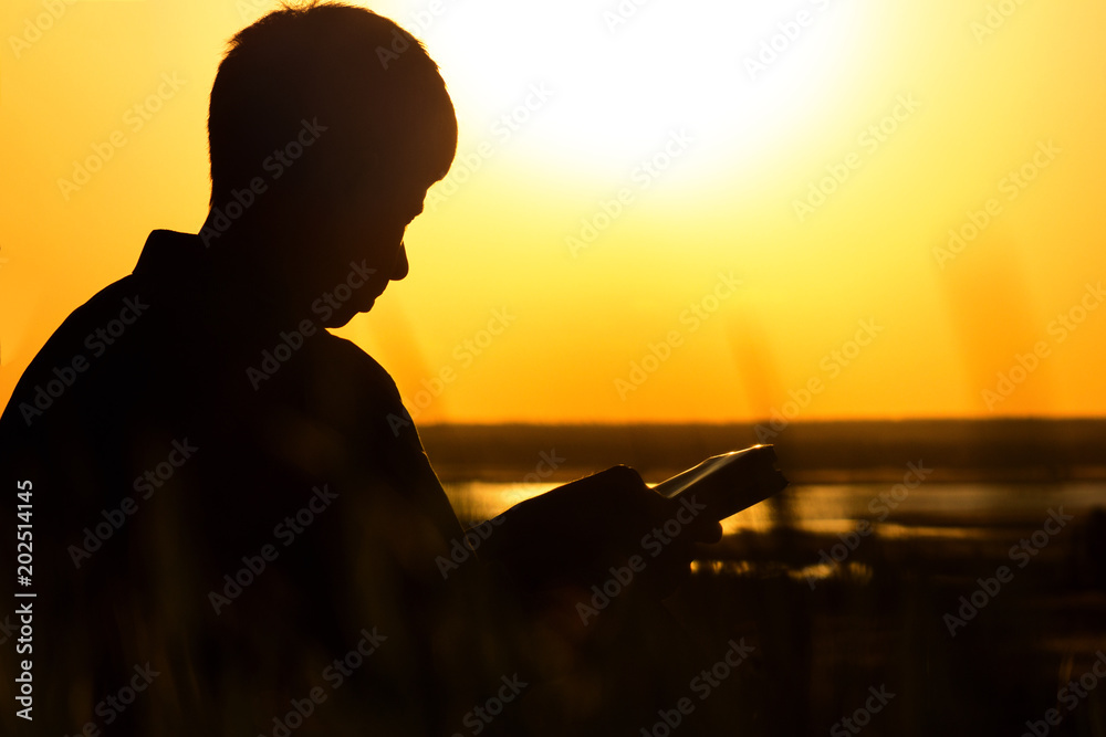 silhouette of a man reading the Bible in the field, male praying to God in nature, the concept of religion and spirituality