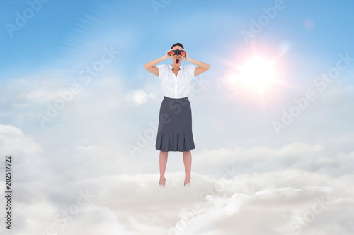 Shocked elegant businesswoman looking through binoculars against blue sky with white clouds