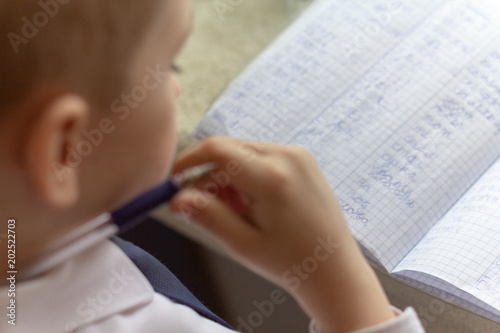 Home education. Home work after school. Boy  with pen writing english words by hand on traditional white notepad paper.  photo