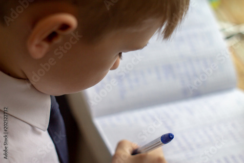 Home education. Home work after school. Boy  with pen writing english words by hand on traditional white notepad paper.  photo