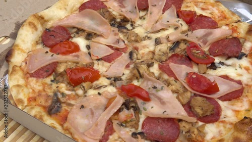 Appetizing pizza with different meats, cheese, ketchup and tomato in a paper box. Cooking. photo