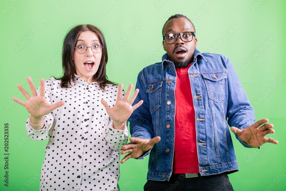 Φωτογραφία African man with European girl raised her hands in surprise standing on green ba