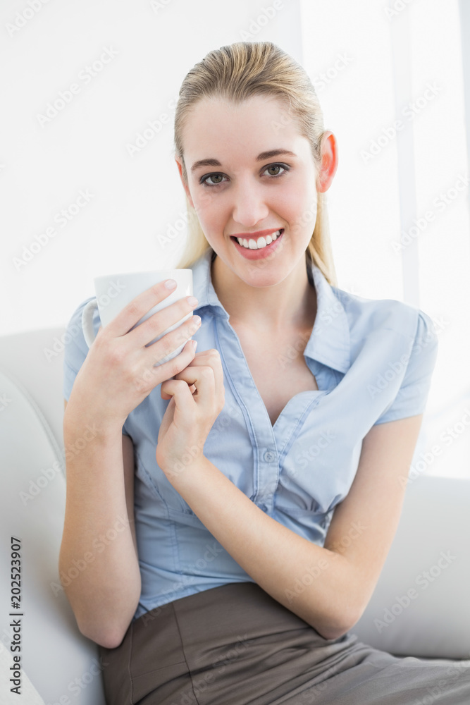 Peaceful blonde businesswoman holding a cup sitting on couch