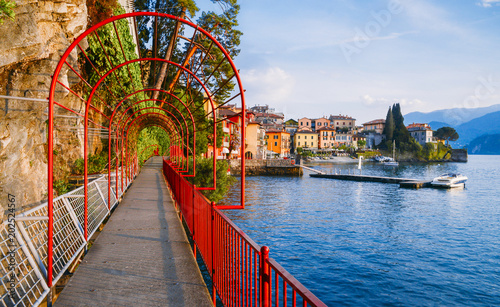 Red garden arch on coastline leading towards the beautiful and historic city of Varenna on the edge of Lake Como in the northern Italian region of Lombardy photo