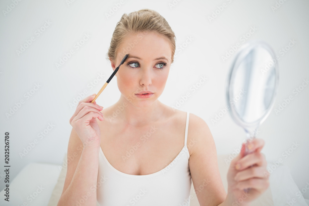 Natural calm blonde holding mirror and using eyebrow brush Natural calm blonde holding mirror and using eyebrow brush