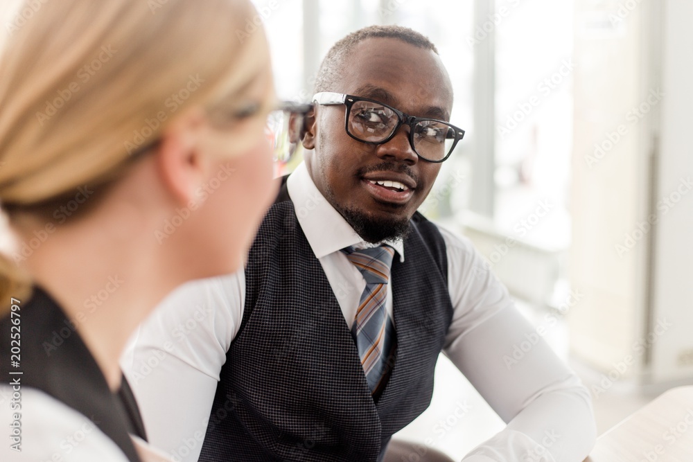 Εκτύπωση καμβά Business girl with glasses talking to African man sitting at table in office