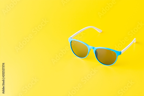 A minimalist arrangement of blue sunglasses on a bright yellow background