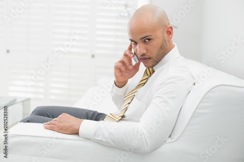 Serious businessman using cellphone on sofa at home