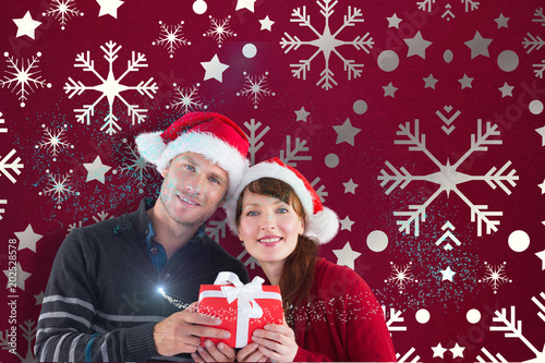 Couple holding a christmas gift against snowflake wallpaper pattern