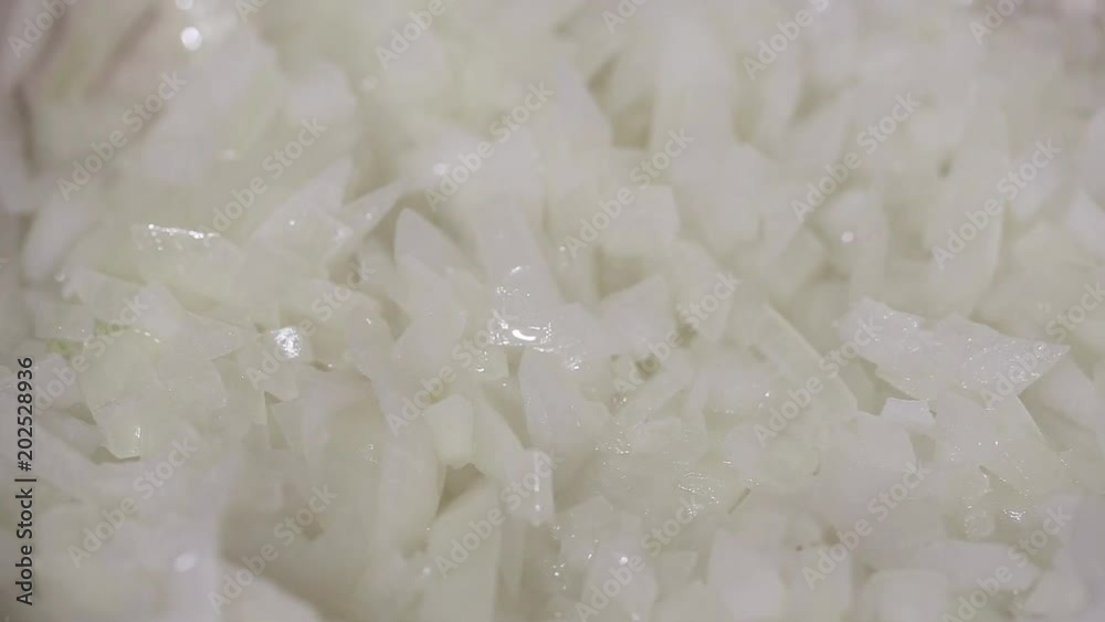 chopped raw onions are fried in a frying pan, onions are hampered with a spatula chopped raw onions are fried in a frying pan, onions are hampered with a spatula