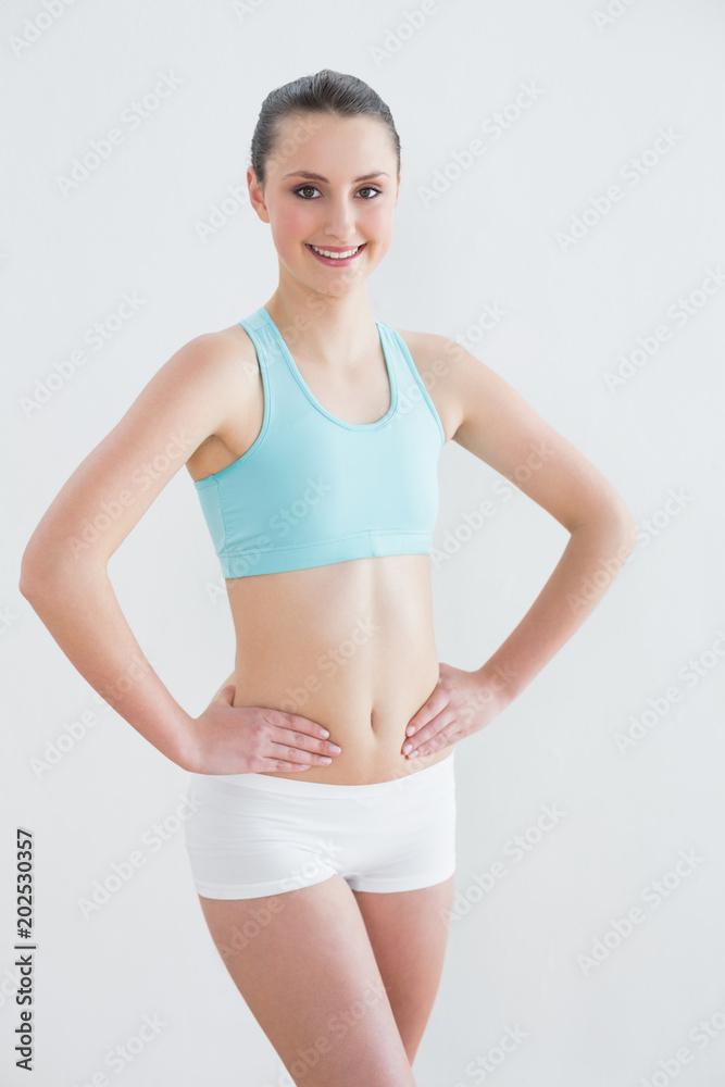Smiling toned woman with hands on hips against wall Smiling toned woman with hands on hips against wall
