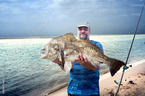 Canvas Print A fisherman is holding a huge fish  black drum (Pogonias cromis)  against the sea