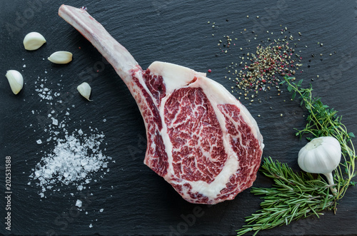Bild auf Leinwand Tomahawk Steak, roh mit Pfeffer, Salz, Knoblauch und Rosmarin auf einer schwarze
