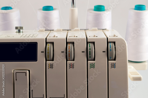 Elements for setting the work of the overlock - thread tension regulators and four coils with white threads on the background. photo