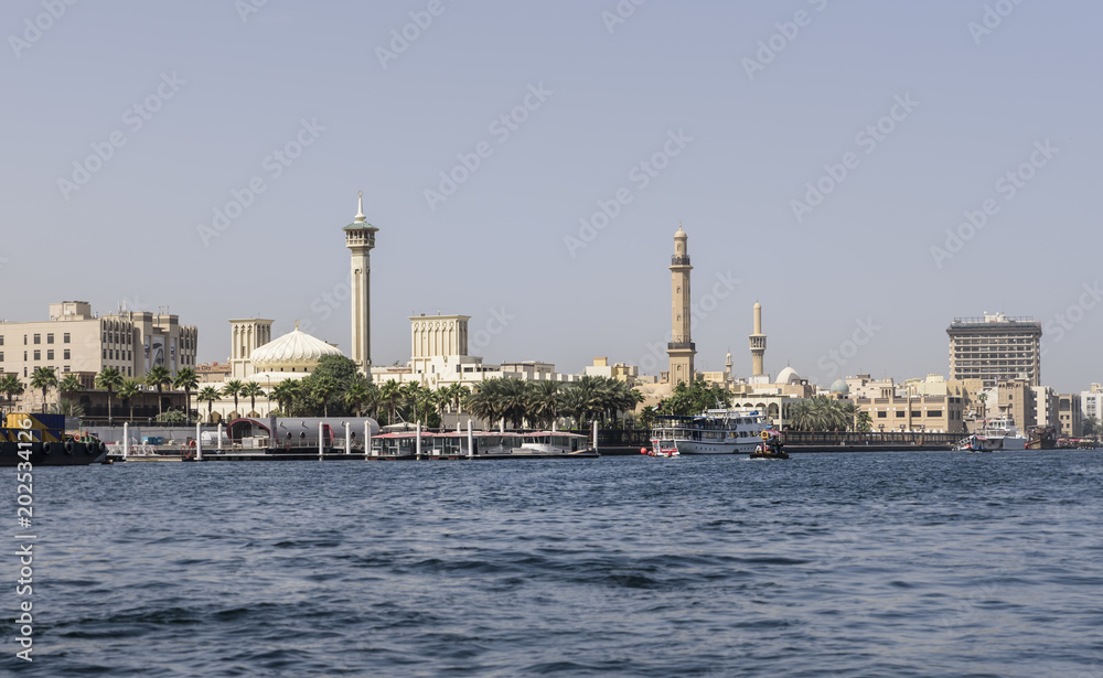 Old Dubai, viewed from the creek, with ancient mosques, along the river bank. The sky is blue and clear