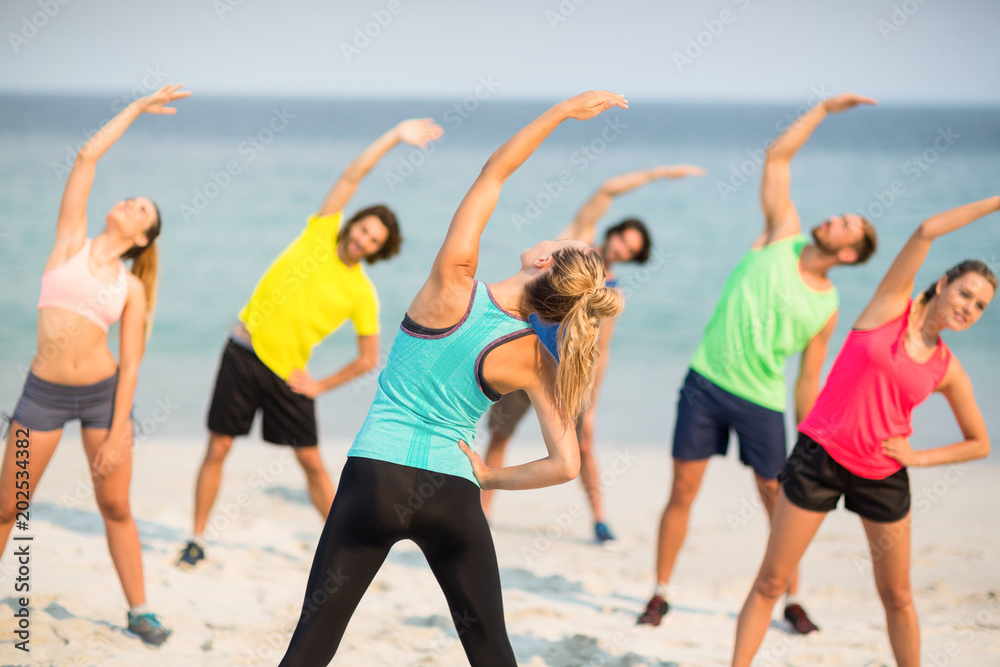 Friends stretching while standing on shore Friends stretching while standing on shore