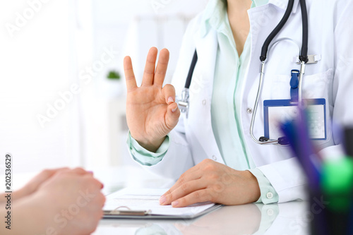 Doctor showing Ok sign to patient while sitting at the desk in hospital office, closeup of human hands. Medicine and health care concept