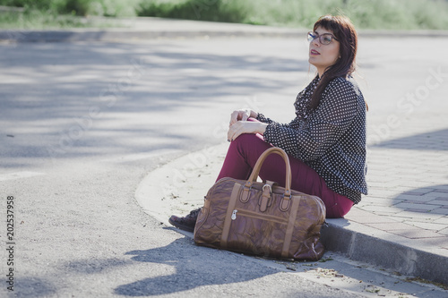 Woman sitting on a sidewalk waiting for a bus photo